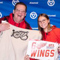 Gentleman smiling and holding up the custom sweatshirt next to young lady holding up "Go Wings" sign